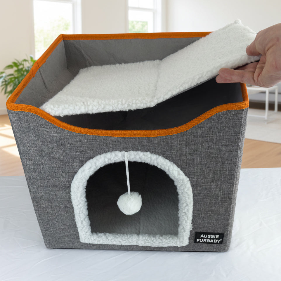Gray pet bed with orange trim and a fluffy white ball, labeled 'Aussie Furbaby', on a light surface.