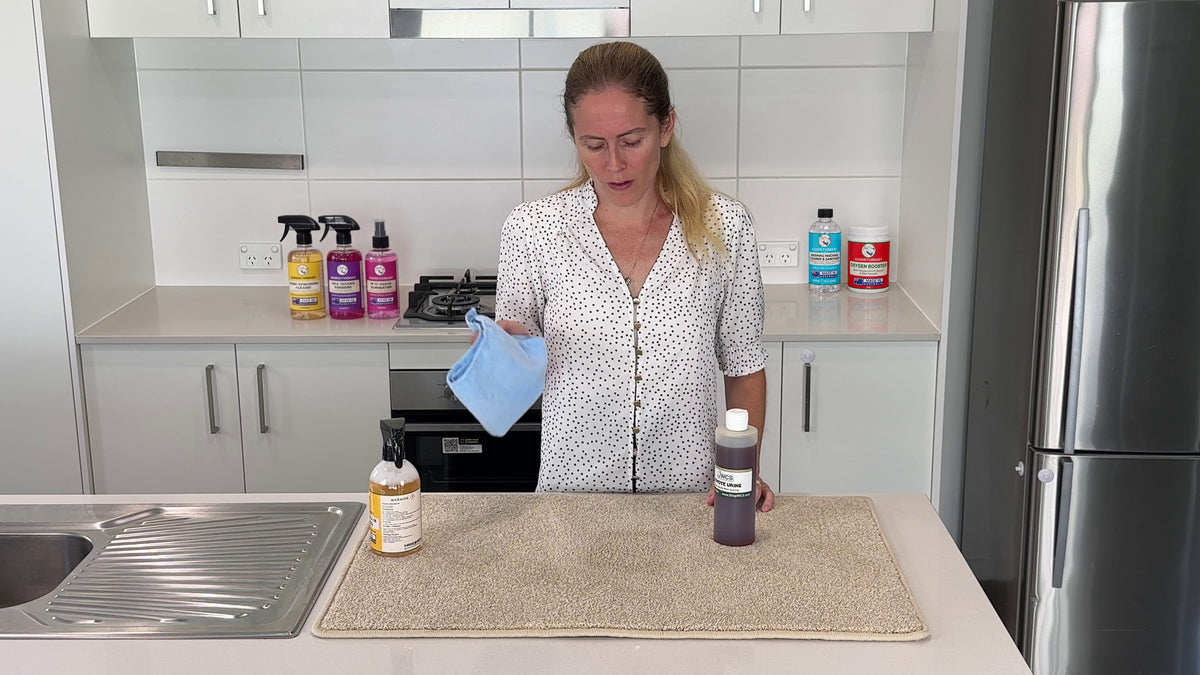 Sammy in her kitchen with the Yellow, Purple and Pink sprays, the washing machine cleaner and the Oxygen Booster on the benches behind her